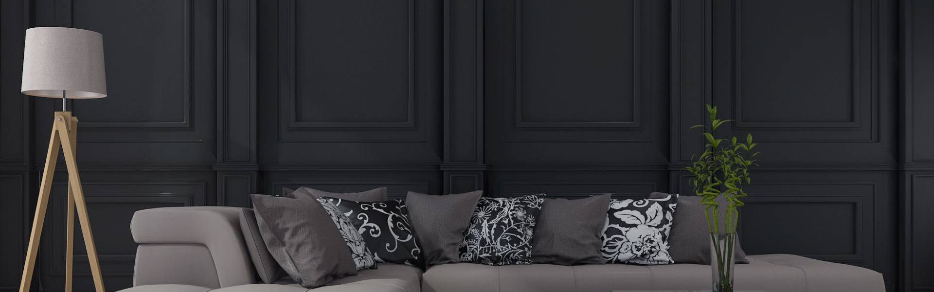 Living room with a wooden tripod lamp on the left, a gray sofa with multiple pillows in the center, and a glass vase with green plants on the right, all set against a dark paneled wall